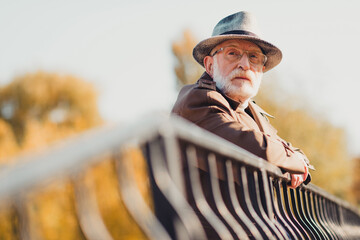 Elderly man enjoying a sunny autumn day outdoors leaning on a railing in a city park surrounded by foliage