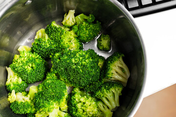 Cooked steamed broccoli heads in steel saucepan. Healthy organic vegan food. Macro shot