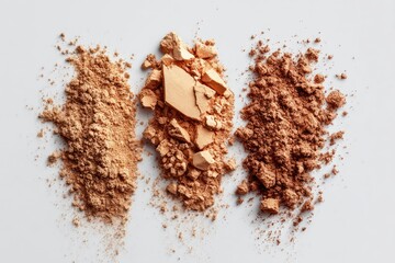 Three shades of loose powder makeup, light beige, medium beige, and light brown, scattered on a light gray background