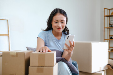 Asian woman using mobile phone among moving boxes for home relocation