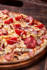 Pizza with ham, salami, cherry tomatoes and mozzarella cheese. Rustic wooden background. Soft focus. Close up.	