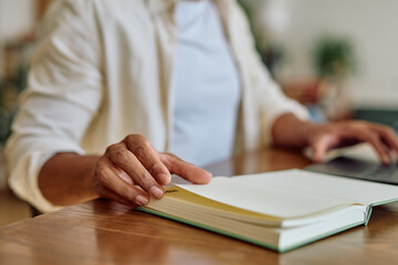 Close up of a manager turning page of open notebook while using laptop computer at home office desk