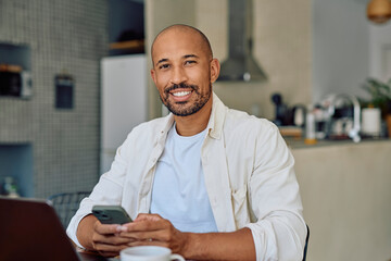 Smiling male freelancer using a smartphone while working remotely in a modern home office, enjoying the convenience of digital communication