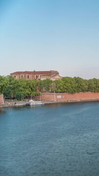 Garonne River and Pont Neuf timelapse with Port de la Daurade in downtown Toulouse, France. This Renaissance arch bridge reflects in the water under a blue sky with clouds. Waterfront with green trees