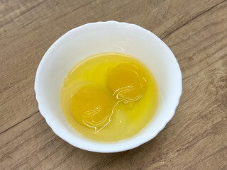 Two raw eggs cracked in a white bowl on wooden table, ready for cooking or baking preparation.