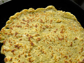 Potato pancake frying in non-stick pan with oil on gas stove, golden brown surface forming during cooking process.