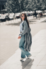 Fototapeta premium Confident woman with long brown hair walking stylishly on a city street in casual attire showcasing urban charm, vertical portrait