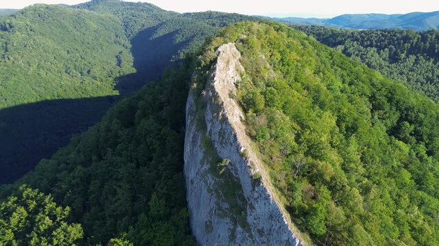 n aerial drone shot captures the powerful beauty of Sivec mountain in Slovakia, where a dramatic, razor-sharp rocky ridge cuts through an expansive, lush green forest.
