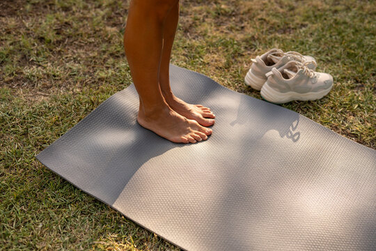 Bare feet on yoga mat next to white running shoes during morning workout in park, symbolizing mindfulness, calm, and healthy active lifestyle