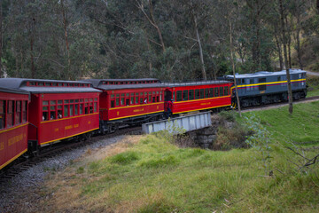 Obraz premium A classic red train crosses a small bridge in a forested landscape. The image is perfect for illustrating travel, tourism, and scenic train routes in the Andes.