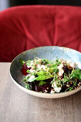 Close-up view of a salad with roasted beetroot, cheese, and fresh herbs, served on a plate in a restaurant on a wooden table.
