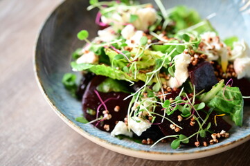 Close-up view of a salad with roasted beetroot, cheese, and fresh herbs, served on a plate in a restaurant on a wooden table.