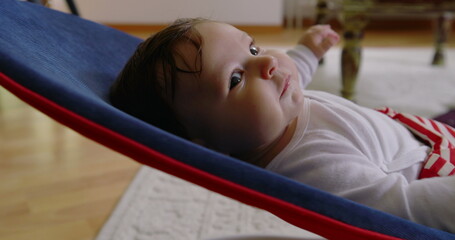 Baby lying in a bouncer, calmly gazing upwards, enjoying a moment of relaxation and comfort in a...