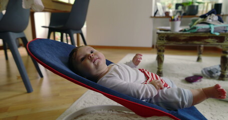 Baby lying in a bouncer, smiling and looking content, enjoying a moment of relaxation and comfort...