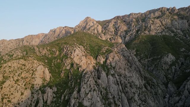 Aerial view of Gulkam gorge in the Chatkal range moves along cliff and saddle as the ravine winds below. Warm dawn color shapes the ridge and stream bed, giving scale and wilderness for travel
