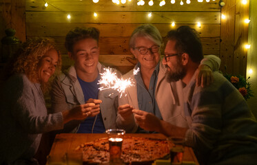 Group of happy multi generation family celebrating together with sparklers at a cozy dinner table, enjoying a warm festive evening under decorative string lights.