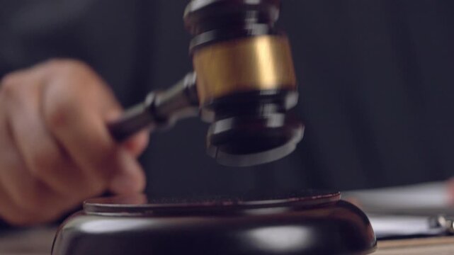 Wooden gavel captured in close-up as judge signs court papers. Representation of authority and courtroom judgment.