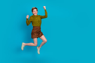 Confident young woman jumps joyfully in retro casual outfit against blue background showcasing vibrant energy and style