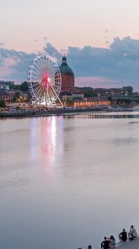 Aerial view of Port de la Daurade park along the Garonne River day to night transition timelapse in Toulouse, France. La Grave Hospital with Saint-Pierre Bridge after sunset with colorful clouds