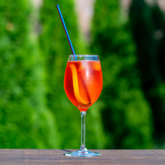 Aperol spritz cocktail in wine glass on a nature background. Classic italian aperitif aperol spritz cocktail with slice of orange. Closeup. Summer refreshing drink with sunlight