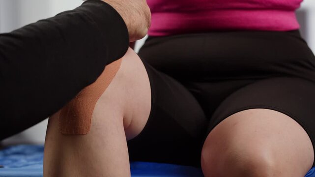 Kinesiology medical taping, doctor Physical therapist applying elastic surgical tape to patient body, treating injured knee young athlete.Post traumatic rehabilitation, sport physical therapy recovery