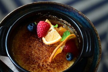 Close-up view of a tasty sweet dessert — crème brûlée served with fresh fruits on a grey background. A delicate caramelized cream dessert with a crunchy top, beautifully styled and served on a table,