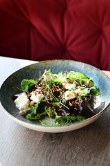 Close-up view of a fresh salad with roasted beetroot and creamy cheese, garnished with greens and herbs.