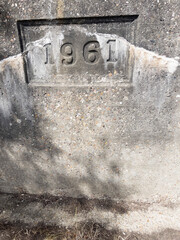 The year '1961' is carved into a weathered concrete surface, its bold numbers standing out amidst the pebbled aggregate and the cracks of time, a faded marker of history.