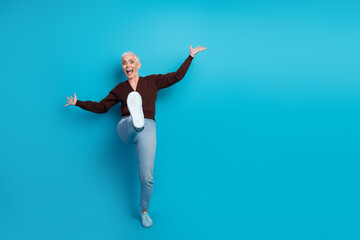 Fototapeta premium Energetic Mature Woman Having Fun with Playful Gesture on a Vibrant Blue Background