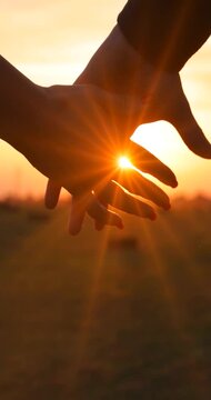 Close-up of the silhouettes of a couple in love holding their hands together, romantic scene at sunset, slow motion. The man and woman have their hands clasped tightly and the golden sun