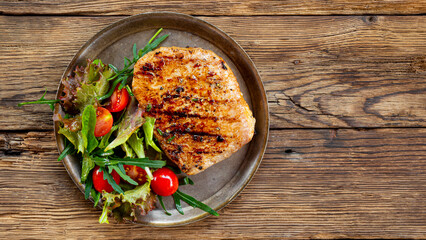 Fried pork steak in plate on wooden background top view, grilled pork with fresh salad