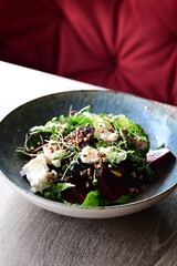 Close-up view of a salad with roasted beetroot, cheese, and fresh herbs, served on a plate in a restaurant on a wooden table.