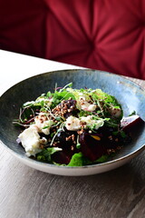 Close-up view of a salad with roasted beetroot, cheese, and fresh herbs, served on a plate in a restaurant on a wooden table.