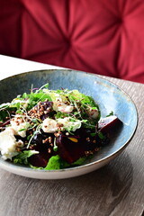 Close-up view of a salad with roasted beetroot, cheese, and fresh herbs, served on a plate in a restaurant on a wooden table.