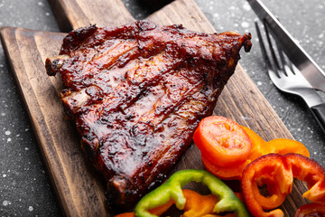 BBQ pork ribs from pork tenderloin with vegetables, ketchup on board and dark background close up