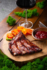 BBQ pork ribs from pork tenderloin with vegetables, cranberry sauce and a glass of red wine on board and wooden background vertical photo