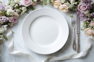 White blank plate on the table, surrounded by a wreath of flowers and with silverware. Gray concrete background. Floral spring display. Minimalist table setting for menu mockup, elegant dining idea