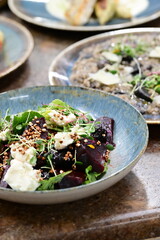 Close-up view of a salad with roasted beetroot, cheese, and fresh herbs, served on a plate in a restaurant on a wooden table.
