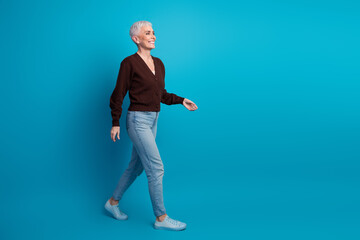 Confident mature woman with short white hair wearing casual fashion, walking gracefully against vibrant blue background