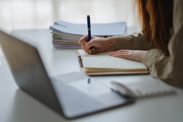 Businesswoman writing notes in notebook while working on laptop in office