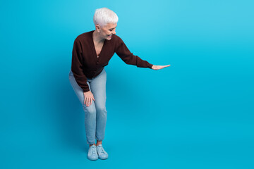Elderly woman with short white hair gesturing with hand against vibrant blue background, showcasing...