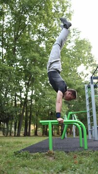 Vertical screen student practices handstand on parallel bars in outdoor park workout area promoting healthy lifestyle strength balance and discipline through modern calisthenics training routine