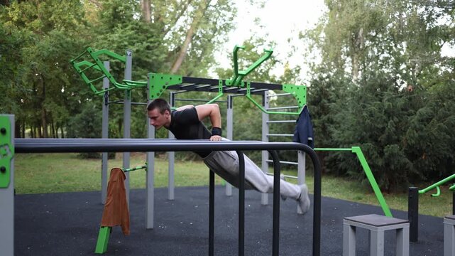 Student trains on parallel bars in outdoor gym holding strong L sit position with focused expression surrounded by trees showing discipline strength and balance in street workout