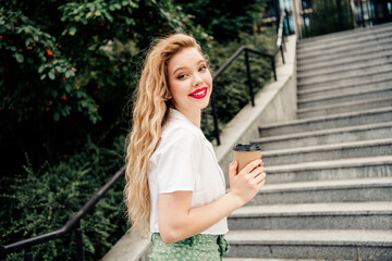 Young woman enjoying a casual outdoor coffee walk in urban sunlight, radiating charm and fashionable spring attire