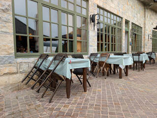 Rustic outdoor cafe terrace with wooden tables and checkered cloths by a stone building. Social gatherings, hospitality, and cultural atmosphere in Drvengrad.