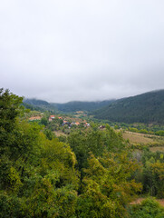 Fototapeta premium Foggy mountains and a valley with small houses and red roofs among green trees. Peaceful rural living and natural beauty in the Balkans.
