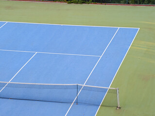 Blue and green tennis court with white lines and net. Sports tourism in mountain village.