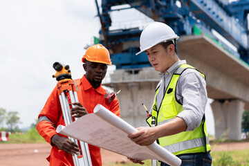 Surveyors and civil engineers using a theodolite and road construction plans to measure and inspect during the building process.