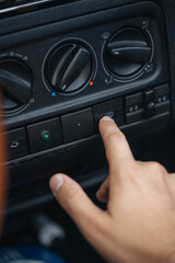 Fototapeta premium A human hand presses a button on the car dashboard climate control panel. Temperature and airflow switches are visible, along with the rear window defrost button inside the vehicle interior.