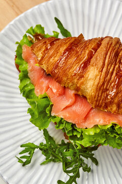 Delicious croissant sandwich with smoked salmon and fresh greens on white plate